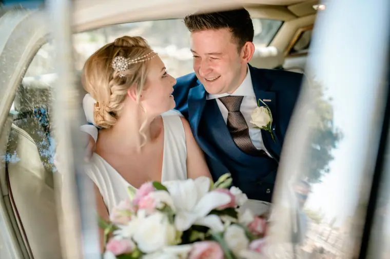 Bride and groom smiling at each other in the back of the wedding car