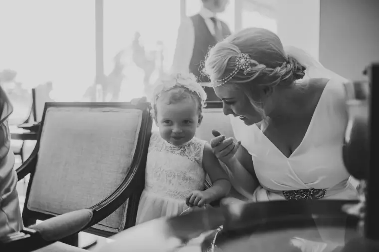 Black-and-white photo of the bride kneeling to greet a toddler in a white dress