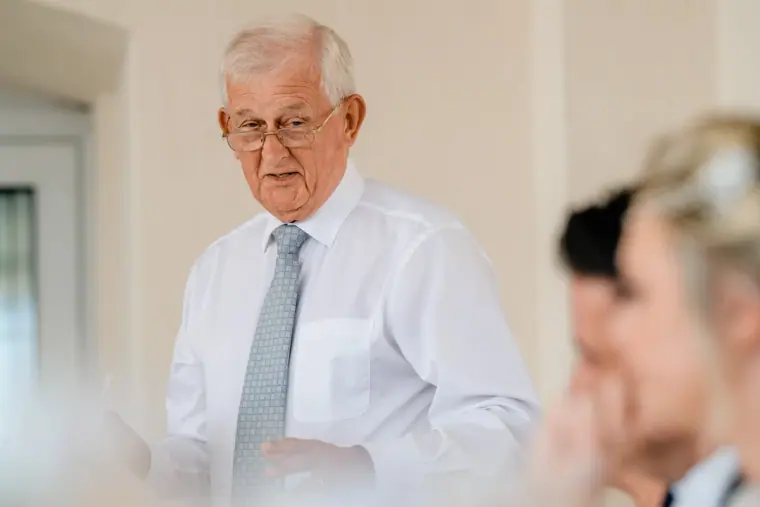 Older man in a shirt and tie giving a speech at the reception