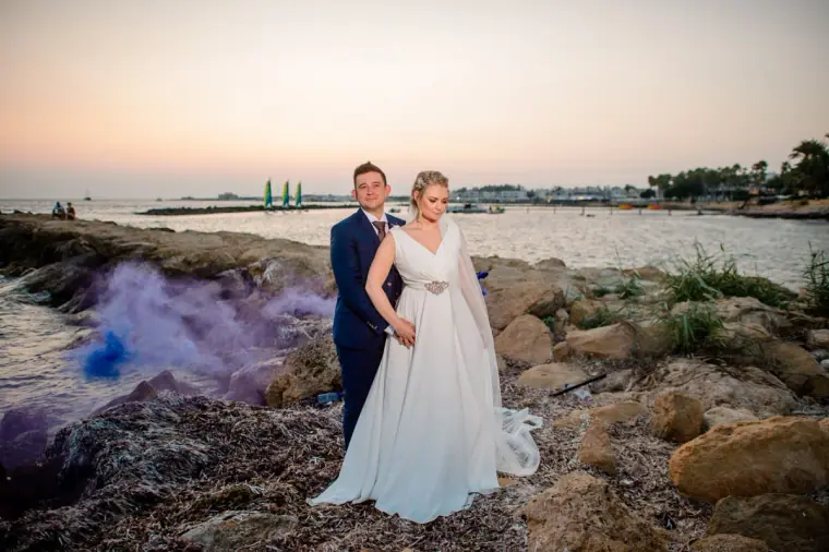 Francesca and Stephen on the rocks with purple smoke at sunset by the sea