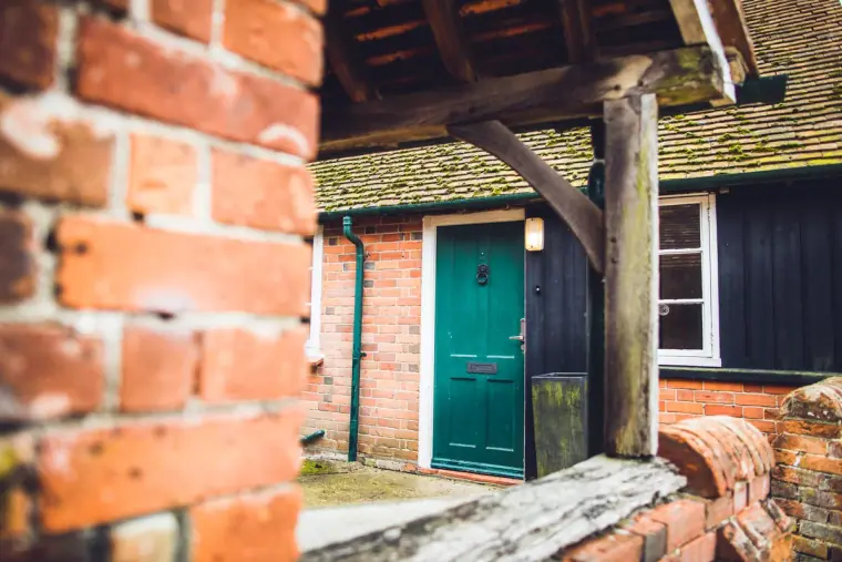 Green front door of a red-brick cottage glimpsed past a brick wall, Wasing Park