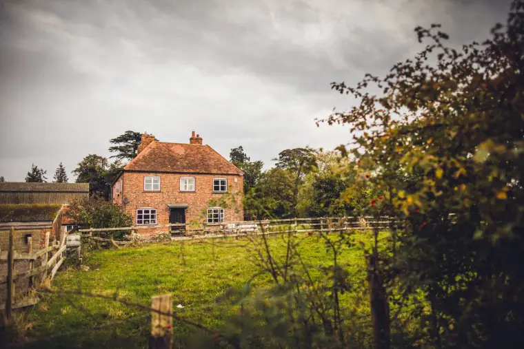 Red-brick farmhouse beyond a paddock fence under grey skies, Berkshire