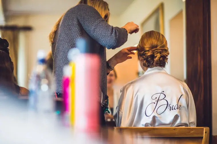Bride in a satin robe having her hair styled on the wedding morning