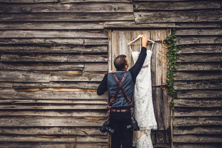 Person hanging the lace wedding dress on a weathered timber barn door