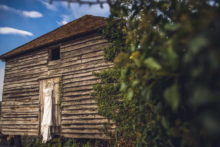 Wedding dress hanging on the door of an old wooden barn at Wasing Park