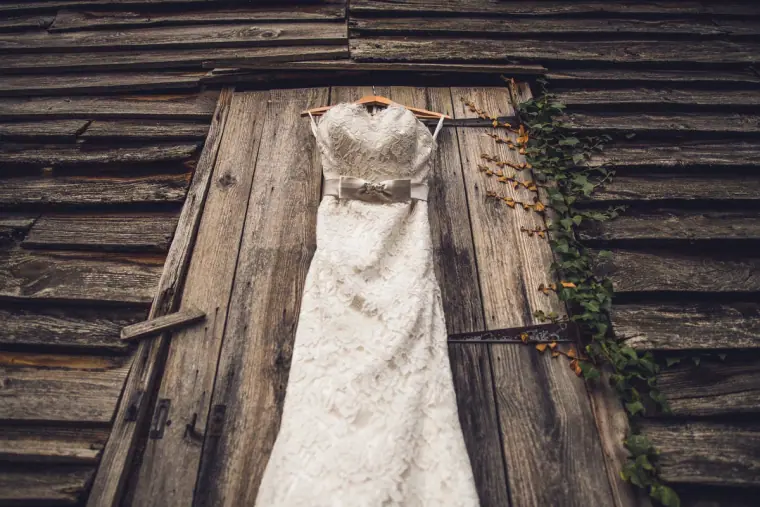 Strapless lace wedding dress hanging against a rustic weathered barn door