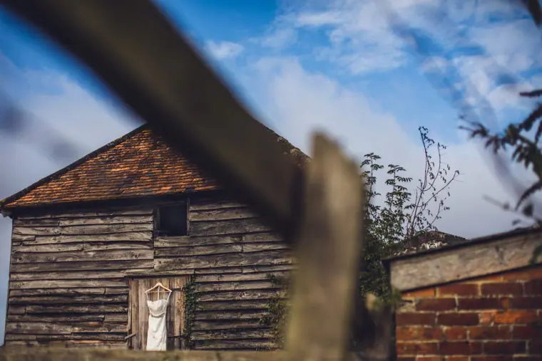 Timber barn with the wedding dress hanging at its door, seen from a low angle
