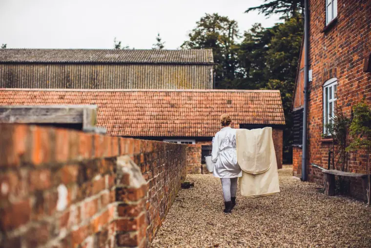 Someone carrying the wedding dress along a gravel path between brick barns