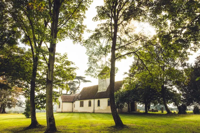 White church at Wasing Park seen between tall trees on the lawn