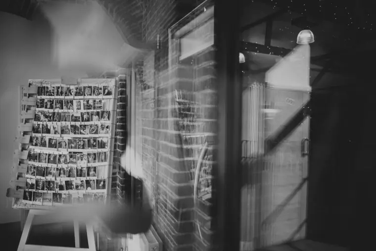 Black-and-white photo of an easel with a board of photographs by a brick doorway