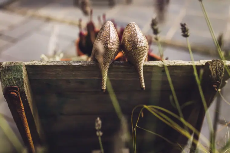 Sparkly gold heels resting on a weathered planter among grasses