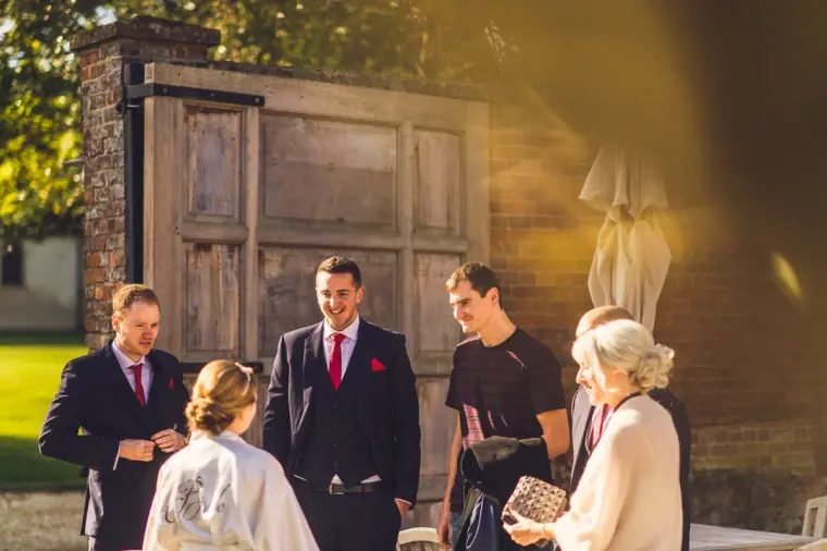 Bride in a robe greeting groomsmen in suits in the courtyard outside a barn