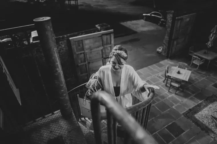 Black-and-white photo of the bride in a robe climbing a staircase, seen from above