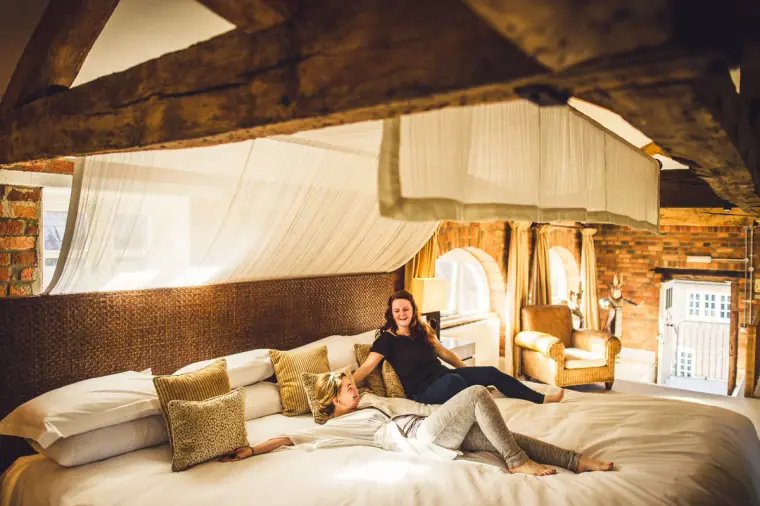 Bridesmaids relaxing on a large canopy bed beneath oak beams