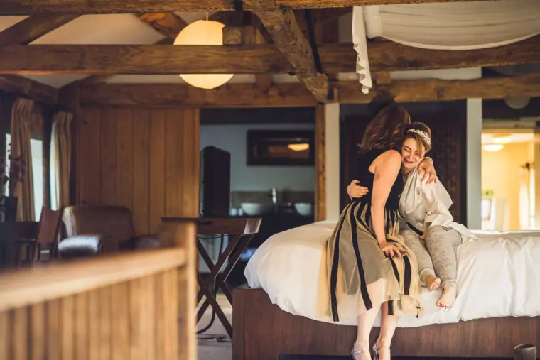 Bridesmaids laughing and bouncing on the bed in the beamed suite
