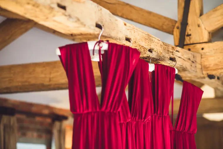 Close-up of red bridesmaid dresses on hangers against old timber beams