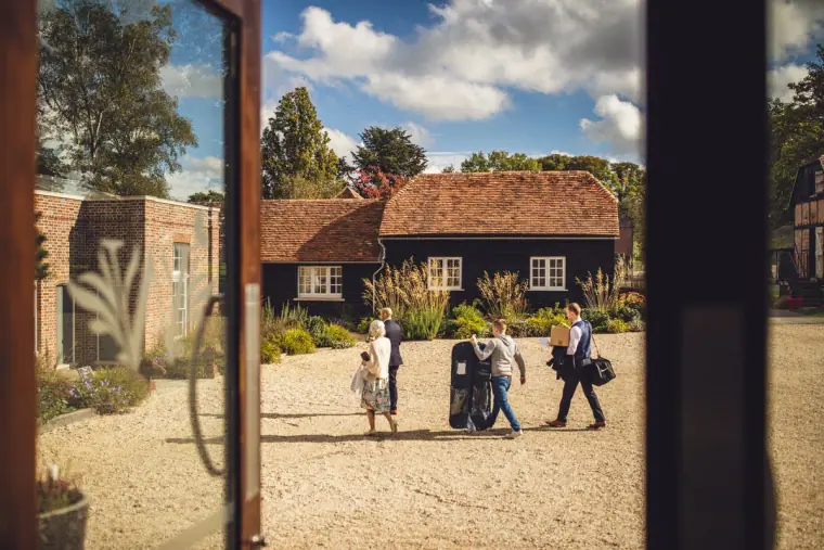 Groomsmen crossing the gravel courtyard towards the barns, seen through a doorway