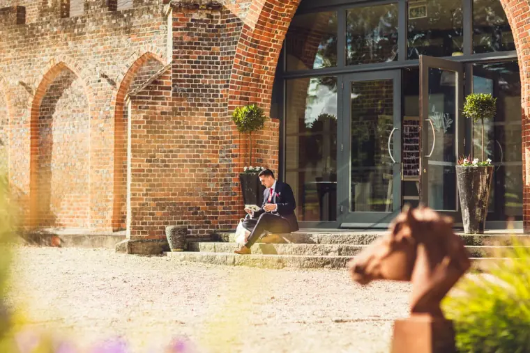 Groomsman sitting on steps beneath a brick archway at Wasing Park