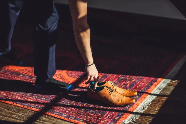 Groom's tan brogues set down on a patterned rug in a shaft of light