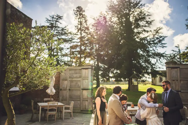 Guests greeting one another in a sunny walled courtyard at Wasing Park