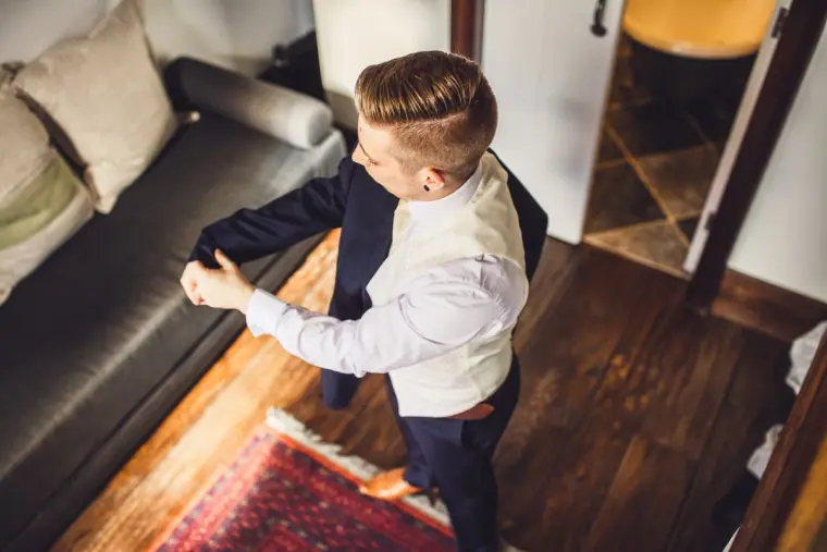 Groom pulling on his jacket in a room with a leather sofa