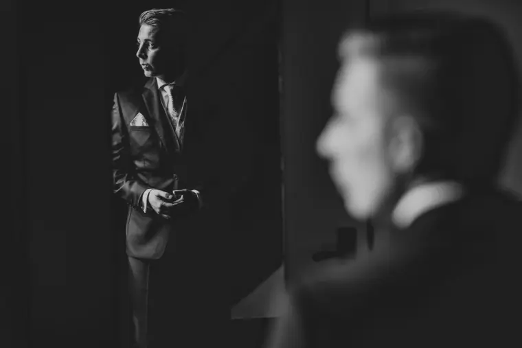 Black-and-white photo of the groom in shadow fastening his cuffs