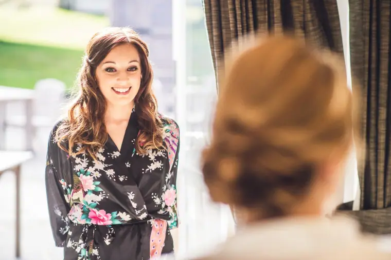 Smiling bridesmaid in a floral robe, seen past the bride's hair