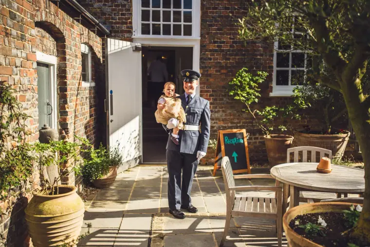 Man in a uniform holding a baby in a brick courtyard at Wasing Park