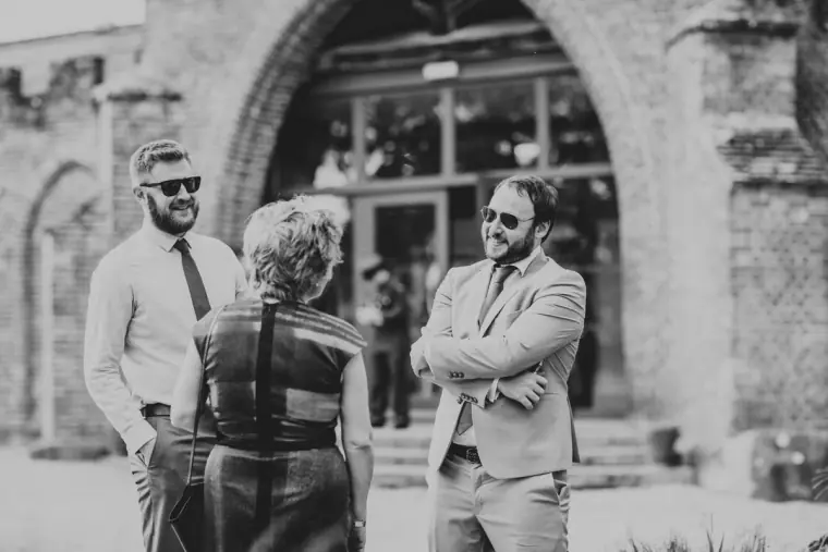 Black-and-white photo of guests in sunglasses chatting outside a brick archway