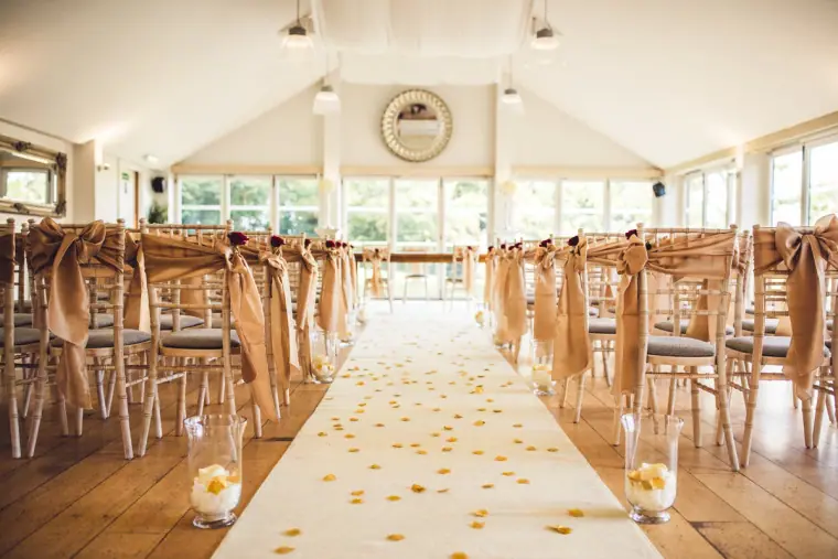 Ceremony room set with chairs, chair sashes and a petal-strewn white aisle at Wasing Park