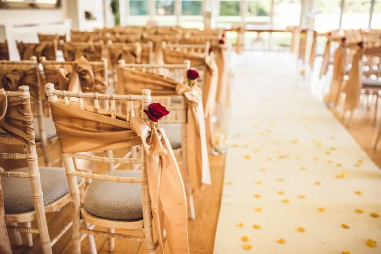 Chairs with ribbon sashes and red roses lining a petal-scattered aisle