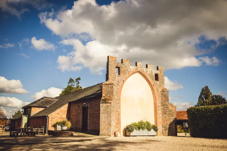 Ruined Gothic brick arch beside the barns under a dramatic sky at Wasing Park