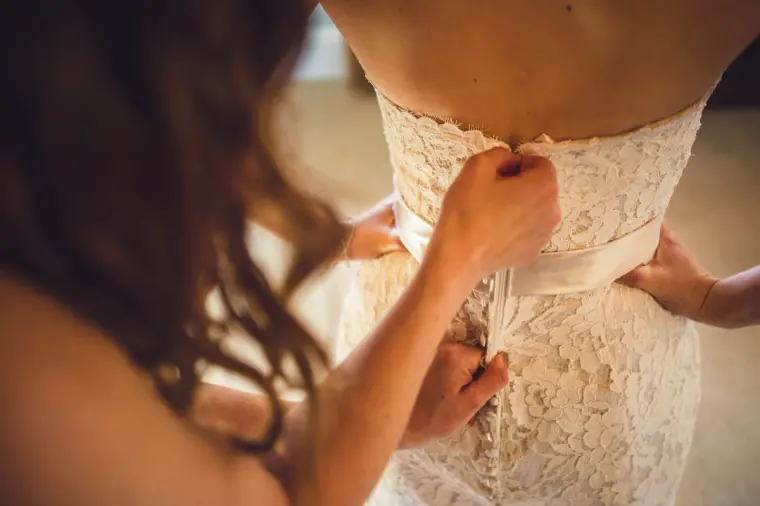 Close-up of hands lacing up the back of the bride's lace dress