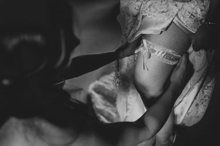 Black-and-white close-up of a lace garter being put on