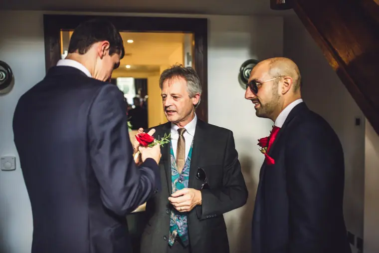 Groomsman pinning a red rose buttonhole on a smiling older man