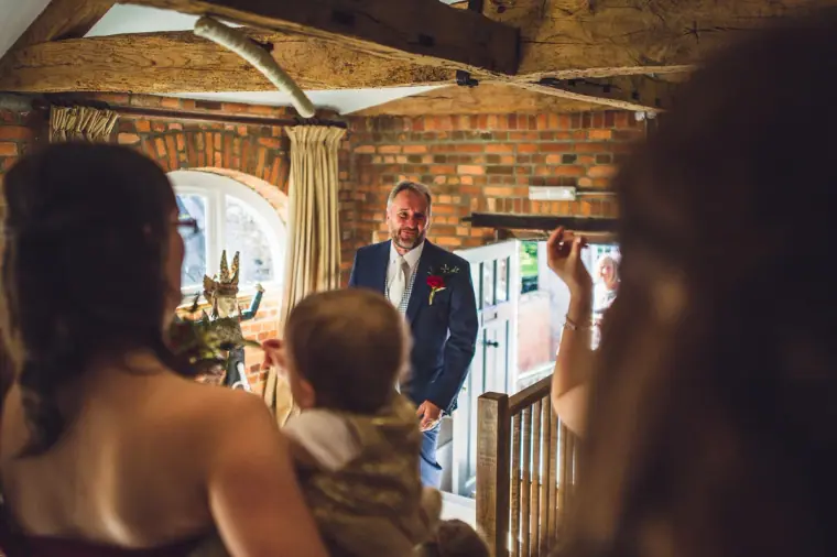 Man in a navy suit arriving in the bridal suite as bridesmaids wait