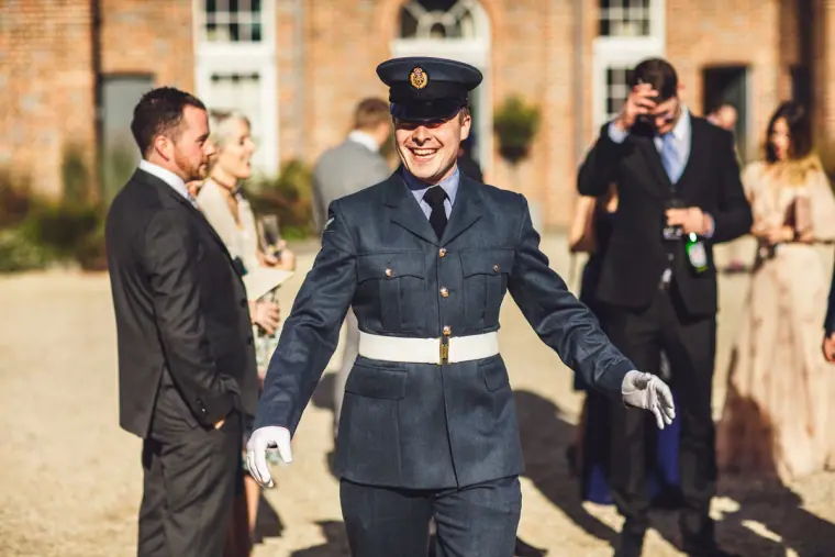 Smiling man in an RAF-style uniform and white gloves greeting guests in the courtyard