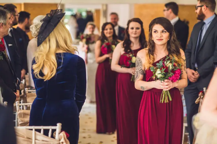 Bridesmaids in burgundy dresses with red bouquets walking down the aisle