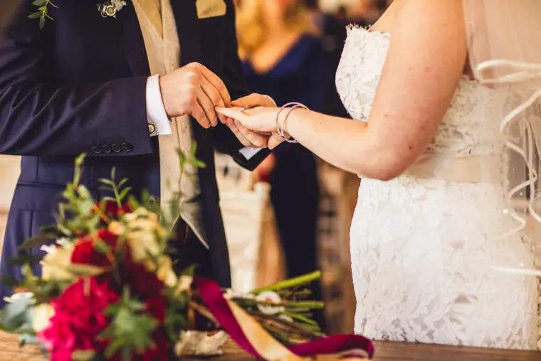 Close-up of the ring exchange beside the red bouquet on the ceremony table