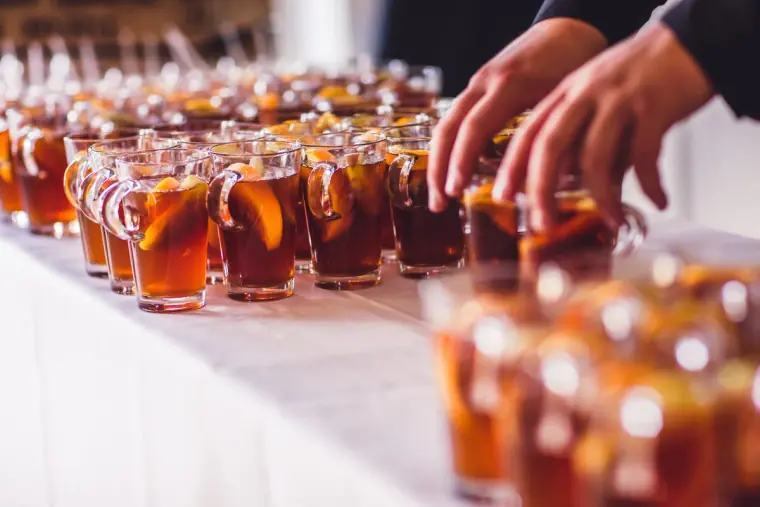 Waiter arranging rows of iced amber drinks with fruit on a long table