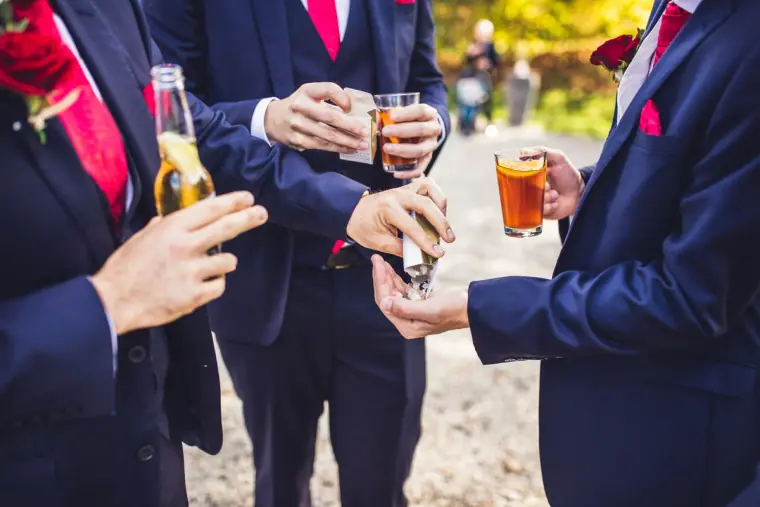 Groomsmen in navy suits clinking bottles and glasses