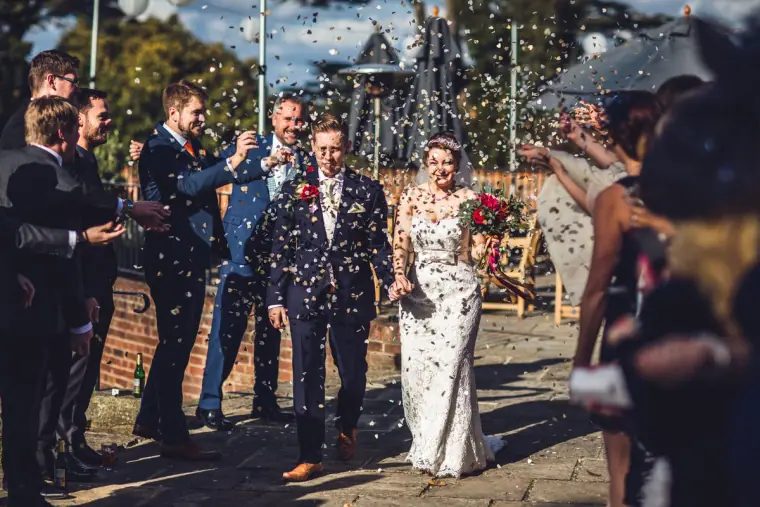 Sarah and Charlie walking through a shower of confetti in the courtyard