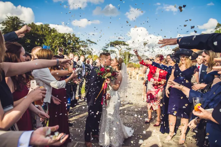 Couple laughing as guests shower them with confetti under a blue sky