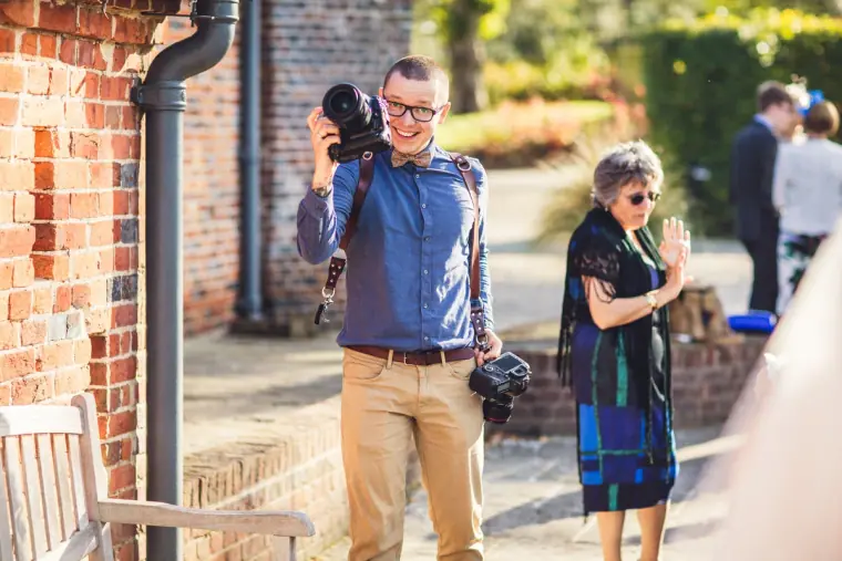 Man with a camera walking past a brick building as guests mingle