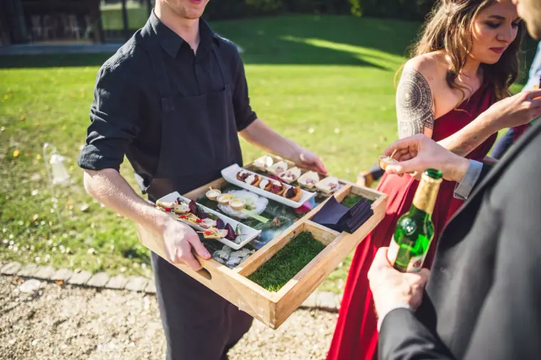 Waiter carrying a tray of canapés across the lawn at Wasing Park