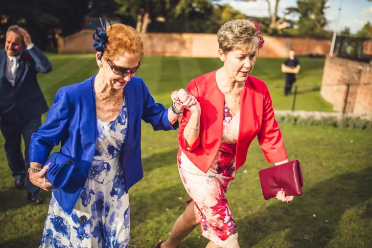 Two women in blue and red jackets walking arm in arm across the lawn