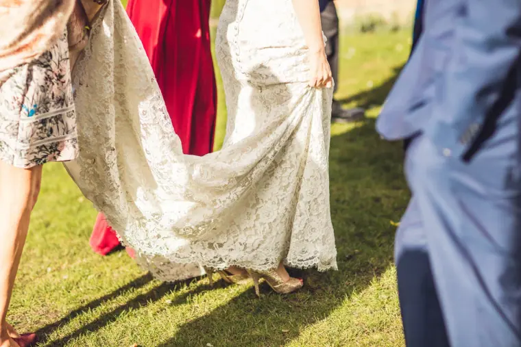 Bridesmaid lifting the lace train of the bride's dress on the grass