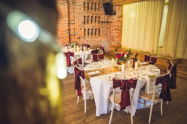 Round tables with burgundy sashes in the brick-walled barn at Wasing Park