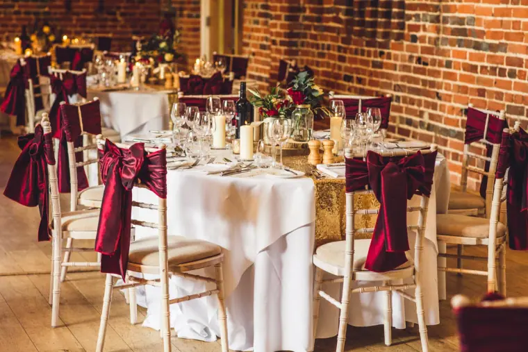 Tables dressed with gold sequin runners and burgundy velvet bows in the barn
