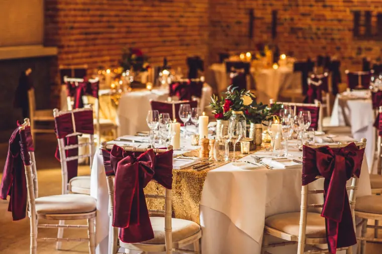 Reception tables with red flowers and candles against an old brick wall